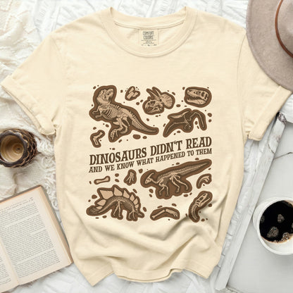 Cream t-shirt with brown dinosaur skeletons and text: "Dinosaurs Didn't Read And We Know What Happened To Them".