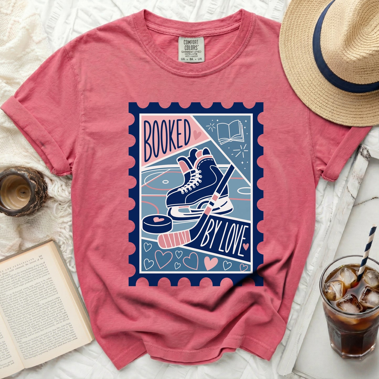 T-shirt with a stamp design featuring ice skates, hockey puck, stick, and text "Booked by Love."