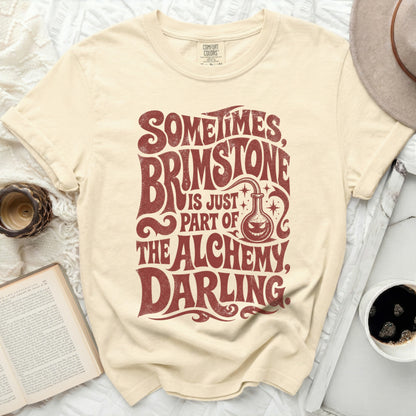 Cream t-shirt with "Sometimes Brimstone is Just Part of the Alchemy, Darling" text.