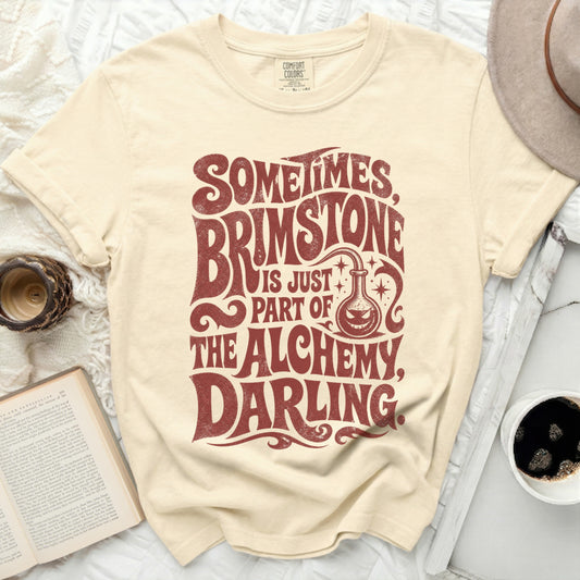 Cream t-shirt with "Sometimes Brimstone is Just Part of the Alchemy, Darling" text.