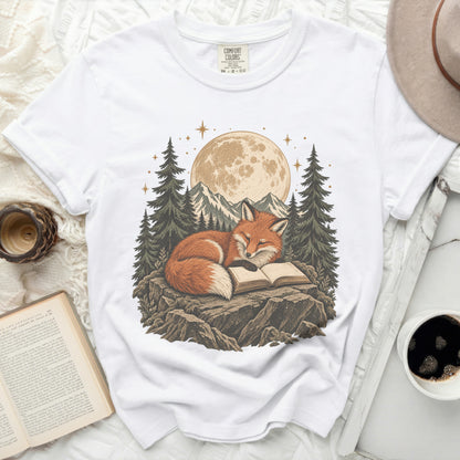 White t-shirt with a graphic of a fox reading a book under a full moon and trees.