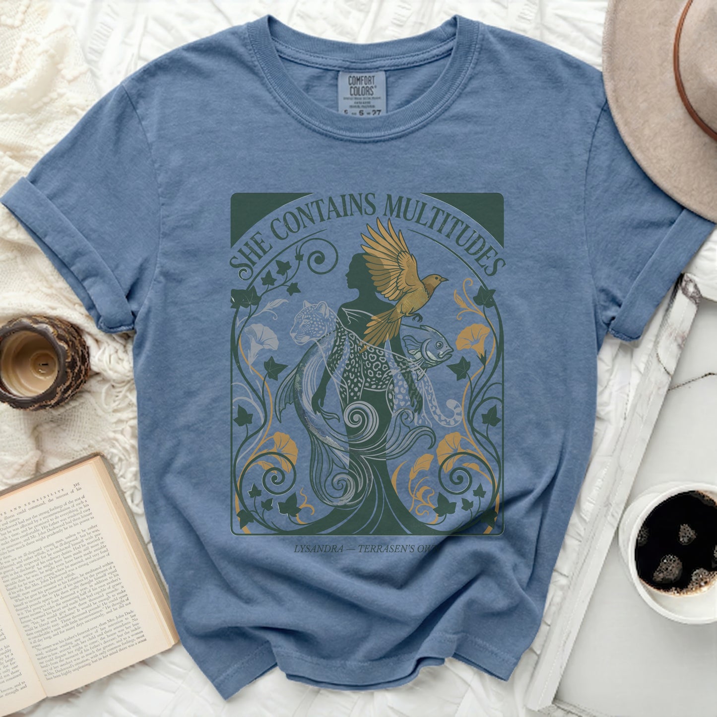 Blue t-shirt with "She Contains Multitudes" text and stylized imagery.