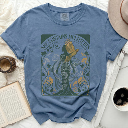 Blue t-shirt with "She Contains Multitudes" text and stylized imagery.