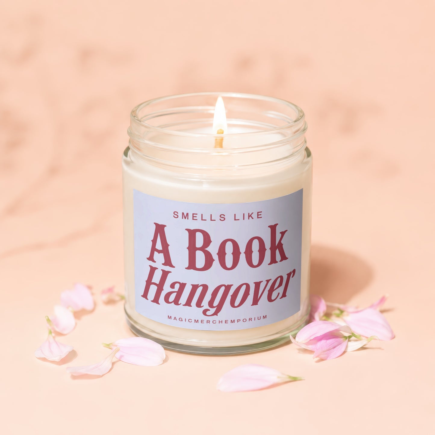 Candle with "Smells Like A Book Hangover" text surrounded by pink petals.