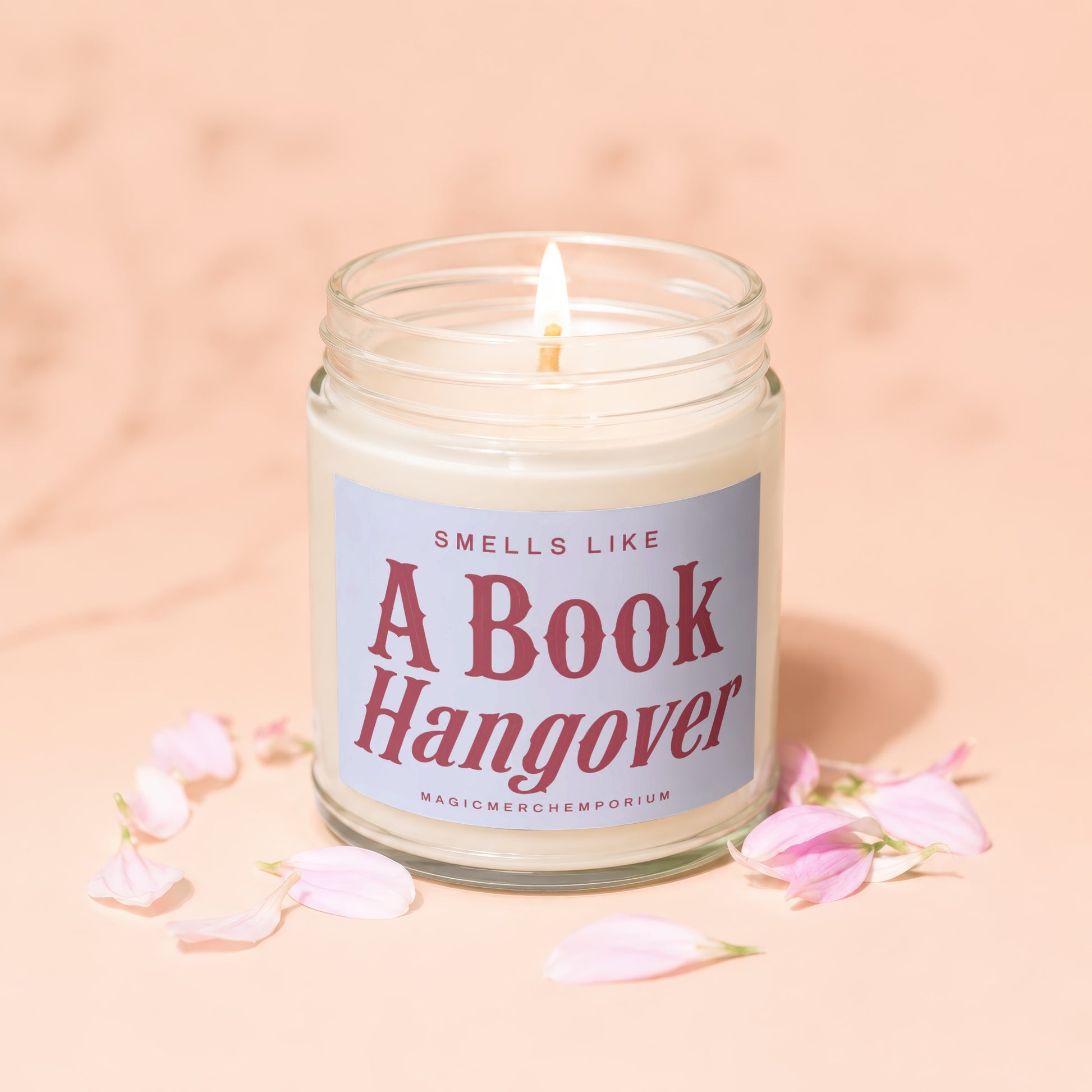 Candle with "Smells Like A Book Hangover" text surrounded by pink petals.