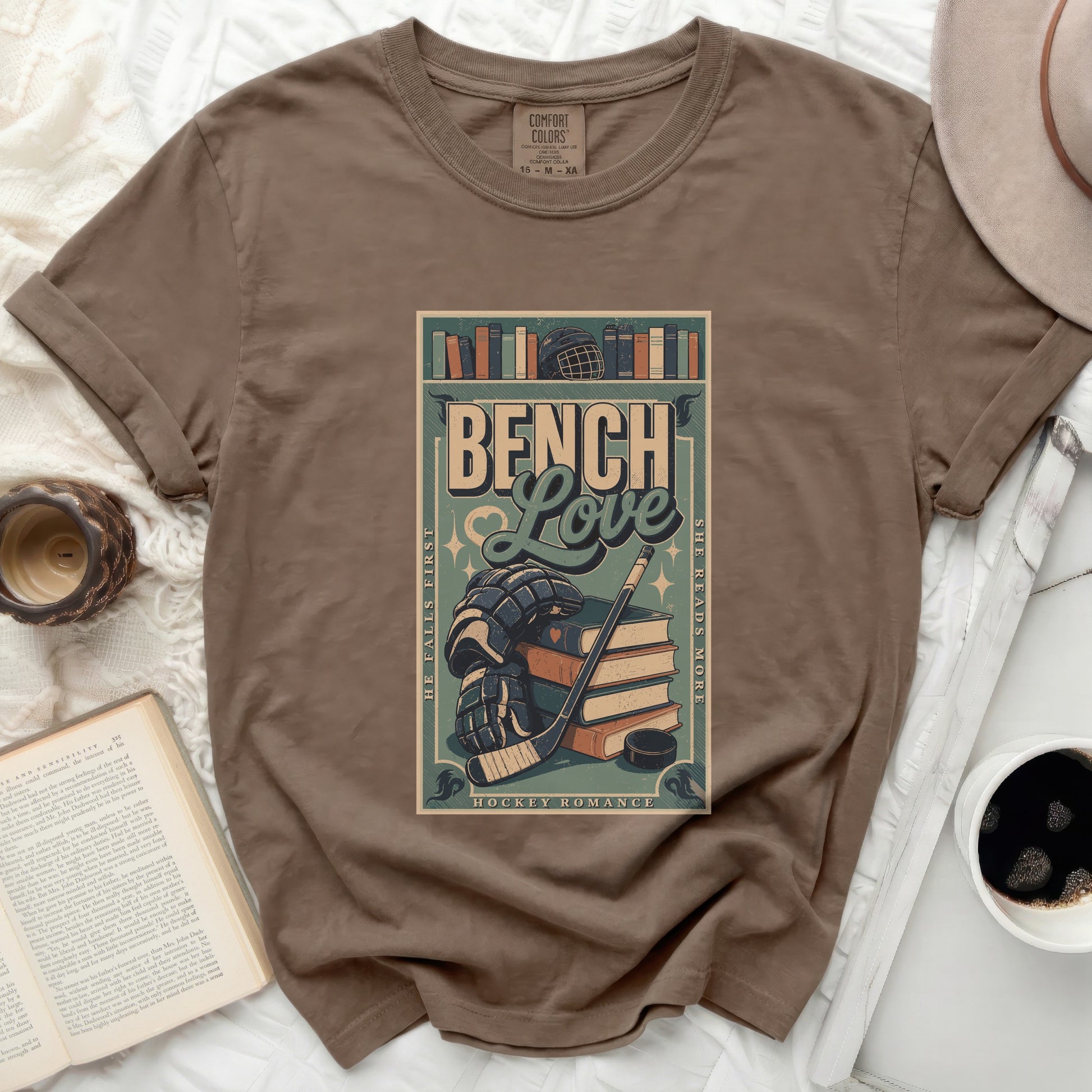 Brown t-shirt with a distressed graphic of books, hockey puck, stick, and skates.