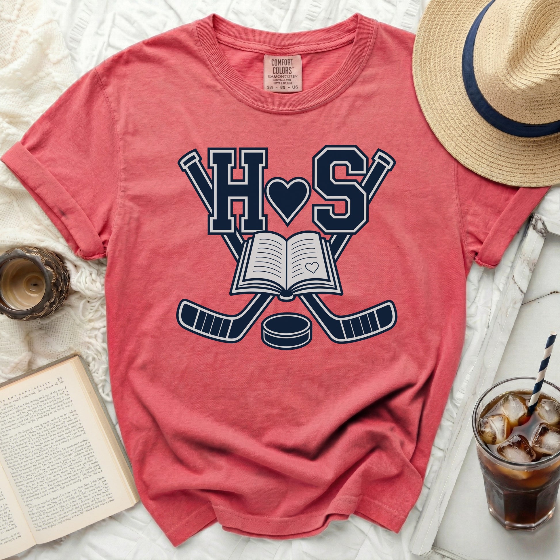 Coral t-shirt with hockey sticks, book, and heart graphic.