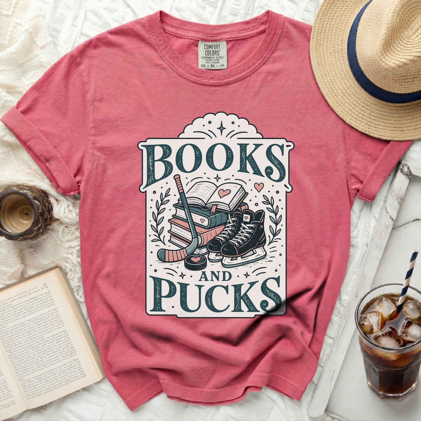 Pink t-shirt with "Books and Pucks" graphic of hockey gear and books.