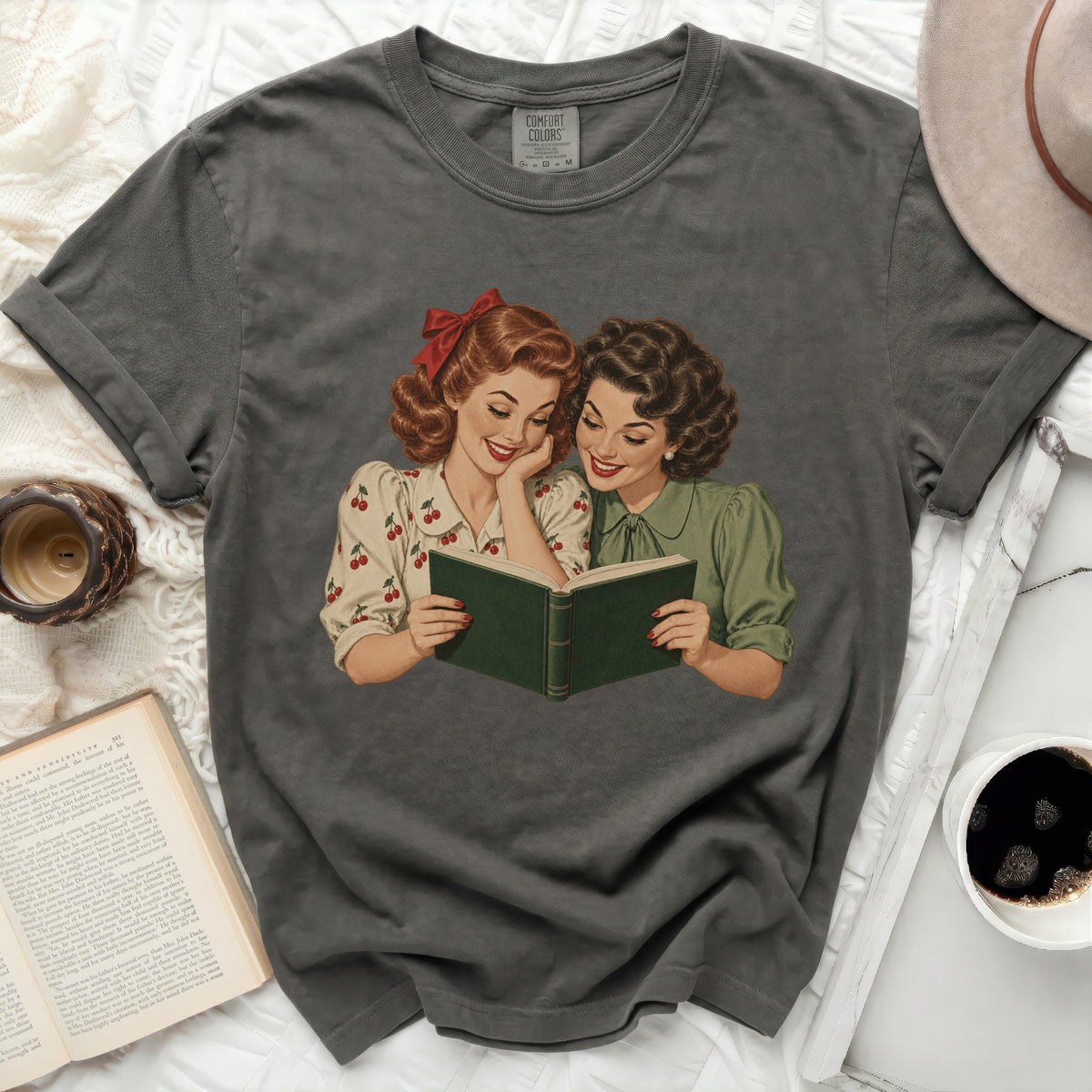 Retro graphic of two women reading a book, printed on a dark grey t-shirt.
