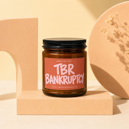 Amber glass candle with black lid, label reads "Smells Like TBR Bankruptcy".