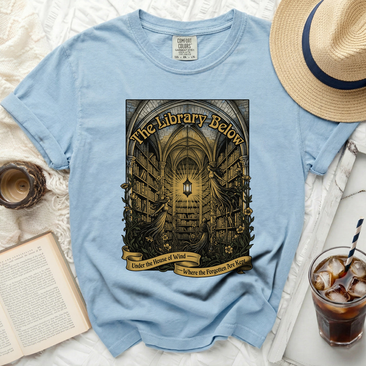 Light blue t-shirt with a graphic of a library, two female figures, and text.