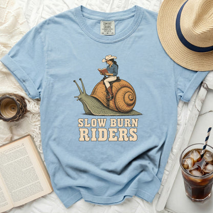 Light blue t-shirt with graphic of woman riding a snail, reading. Text says "SLOW BURN RIDERS."