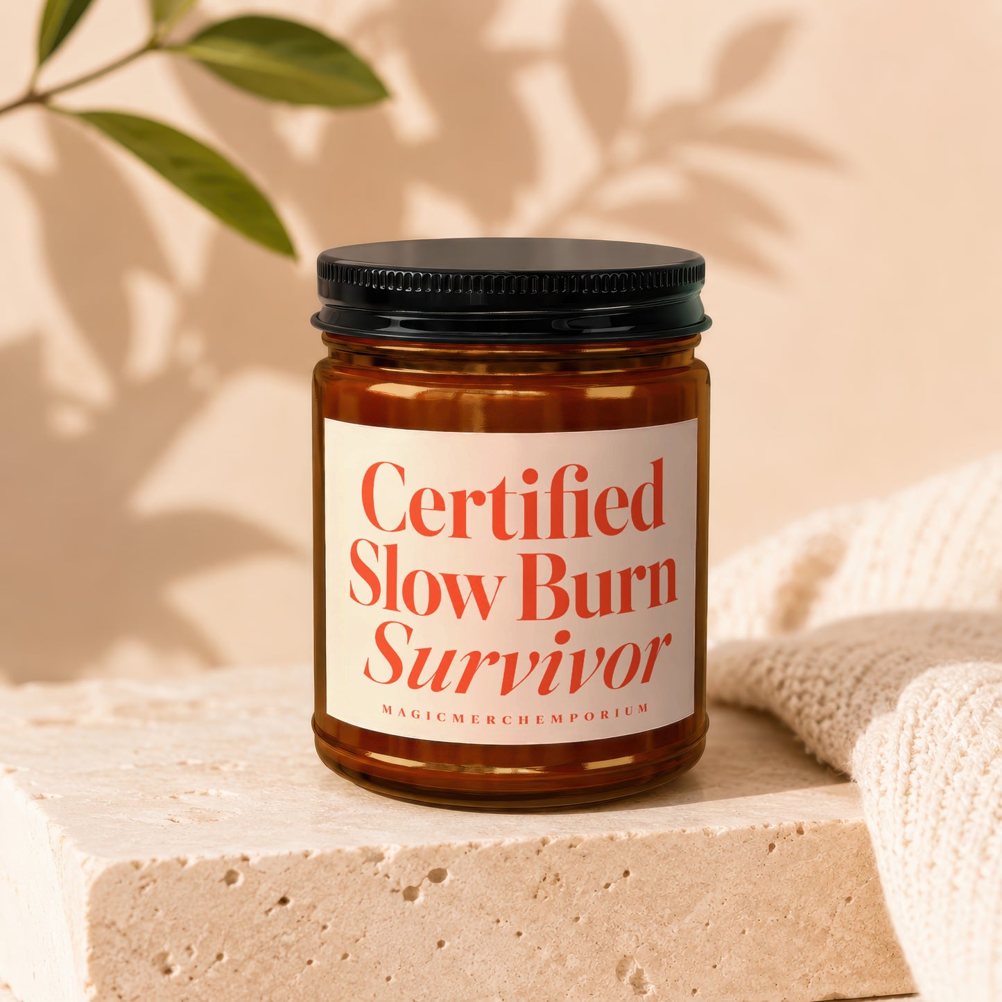 Amber glass candle with black lid, "Certified Slow Burn Survivor" text, on a stone block.