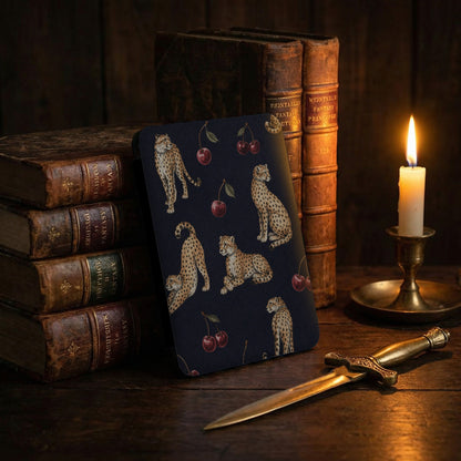 Dark blue patterned journal with cheetahs and cherries, next to old books and candle.