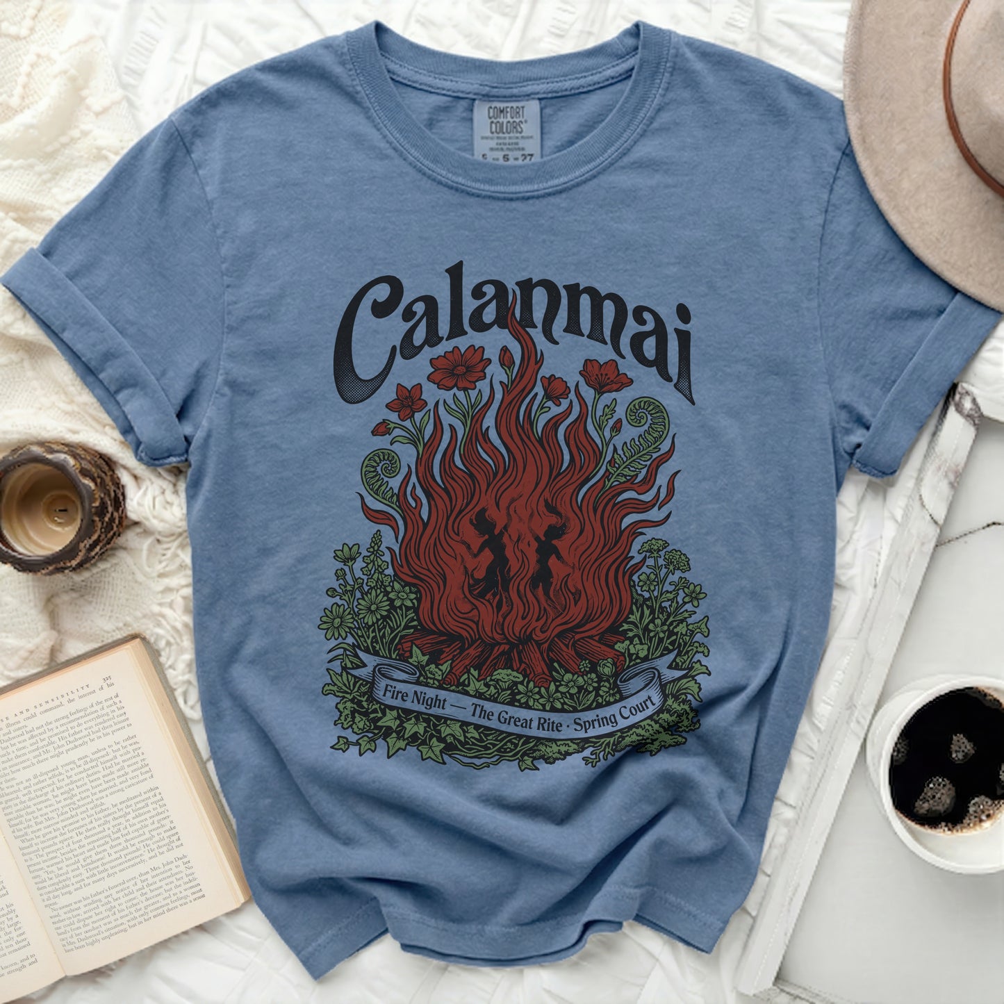 Blue t-shirt with "Calanmai" and a campfire with dancers and flowers graphic.