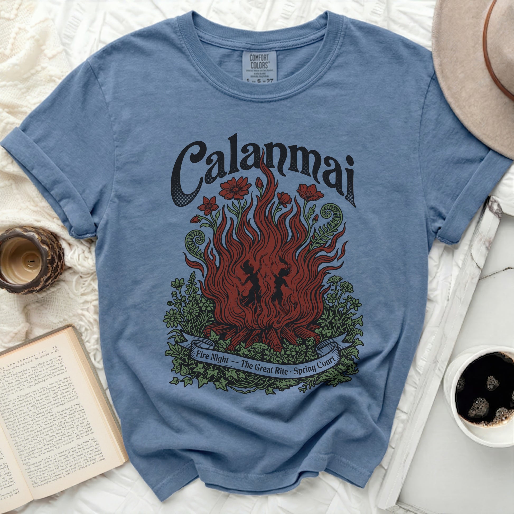 Blue t-shirt with "Calanmai" and a campfire with dancers and flowers graphic.