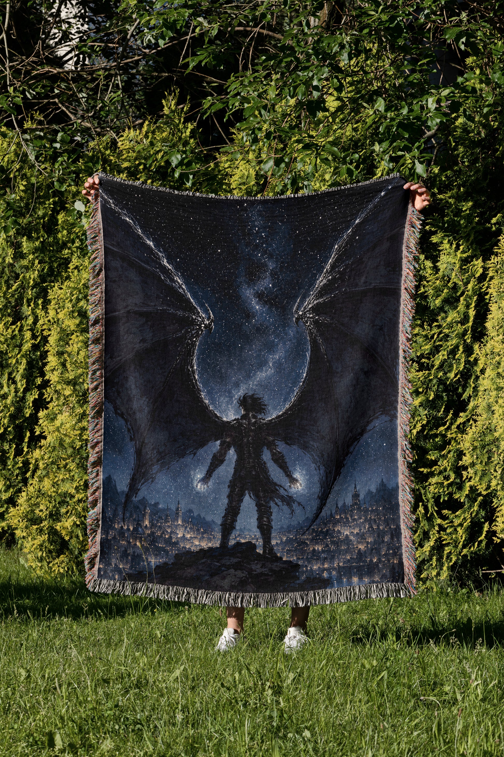 A person is holding up a large blanket with a dragon design on it, standing in a grassy area with trees in the background.
