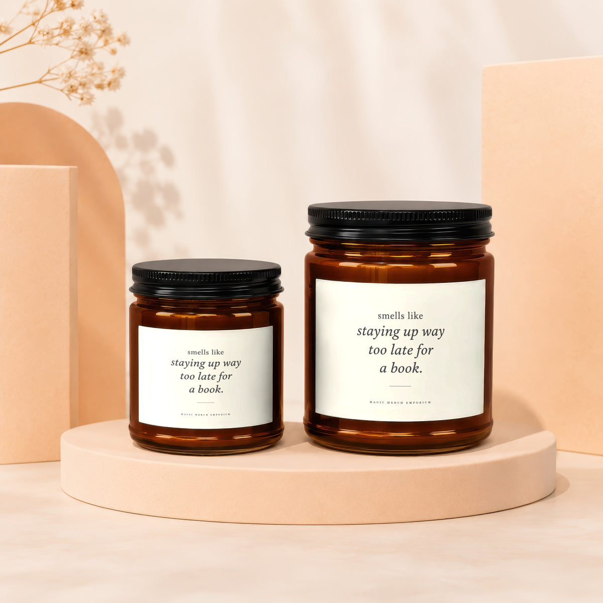 Two amber glass candles with black lids, featuring text "smells like staying up way too late for a book."