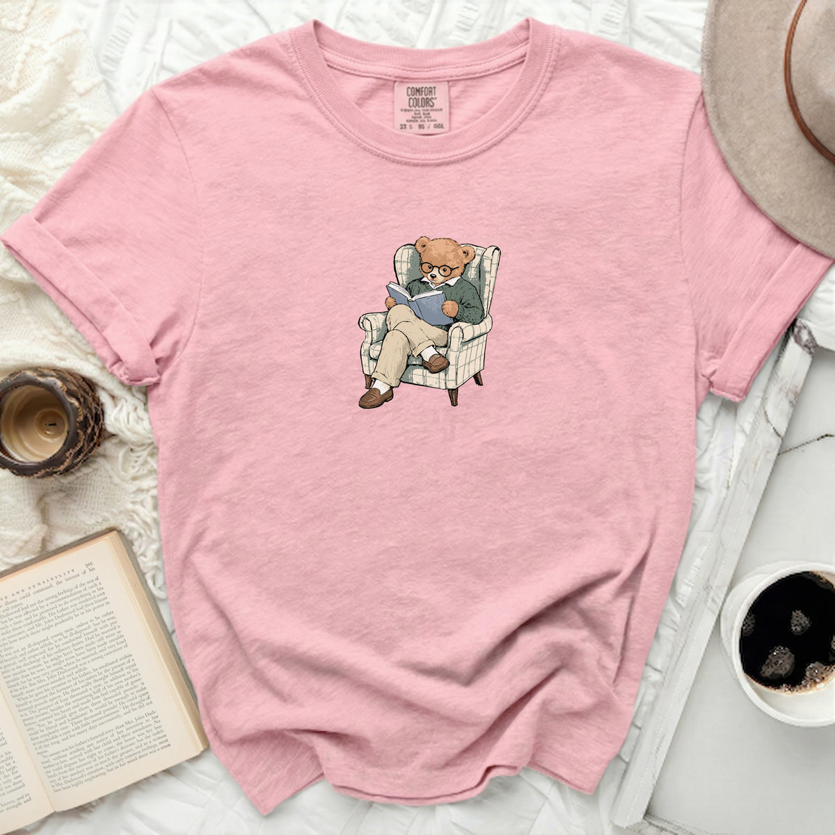 Pink t-shirt with a graphic of a teddy bear reading in an armchair.