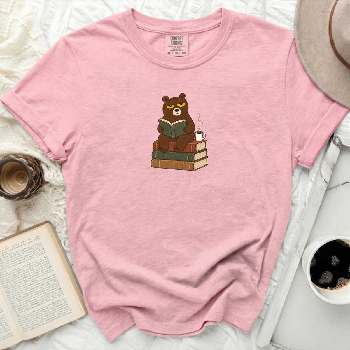 Pink t-shirt with illustration of a grumpy bear reading on books.