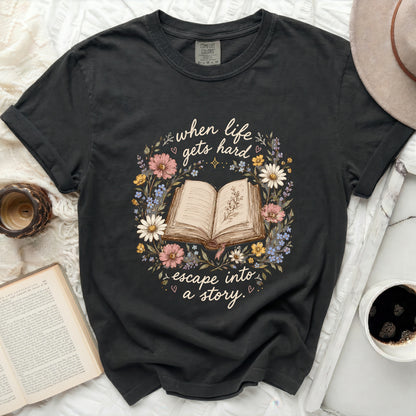 Dark t-shirt with "when life gets hard escape into a story" text and floral book graphic.