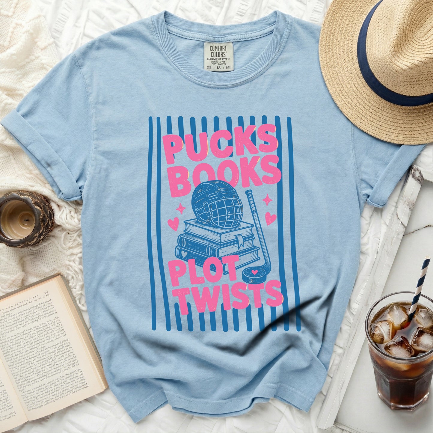 Light blue t-shirt with "Pucks Books Plot Twists" text, hockey gear, and books.