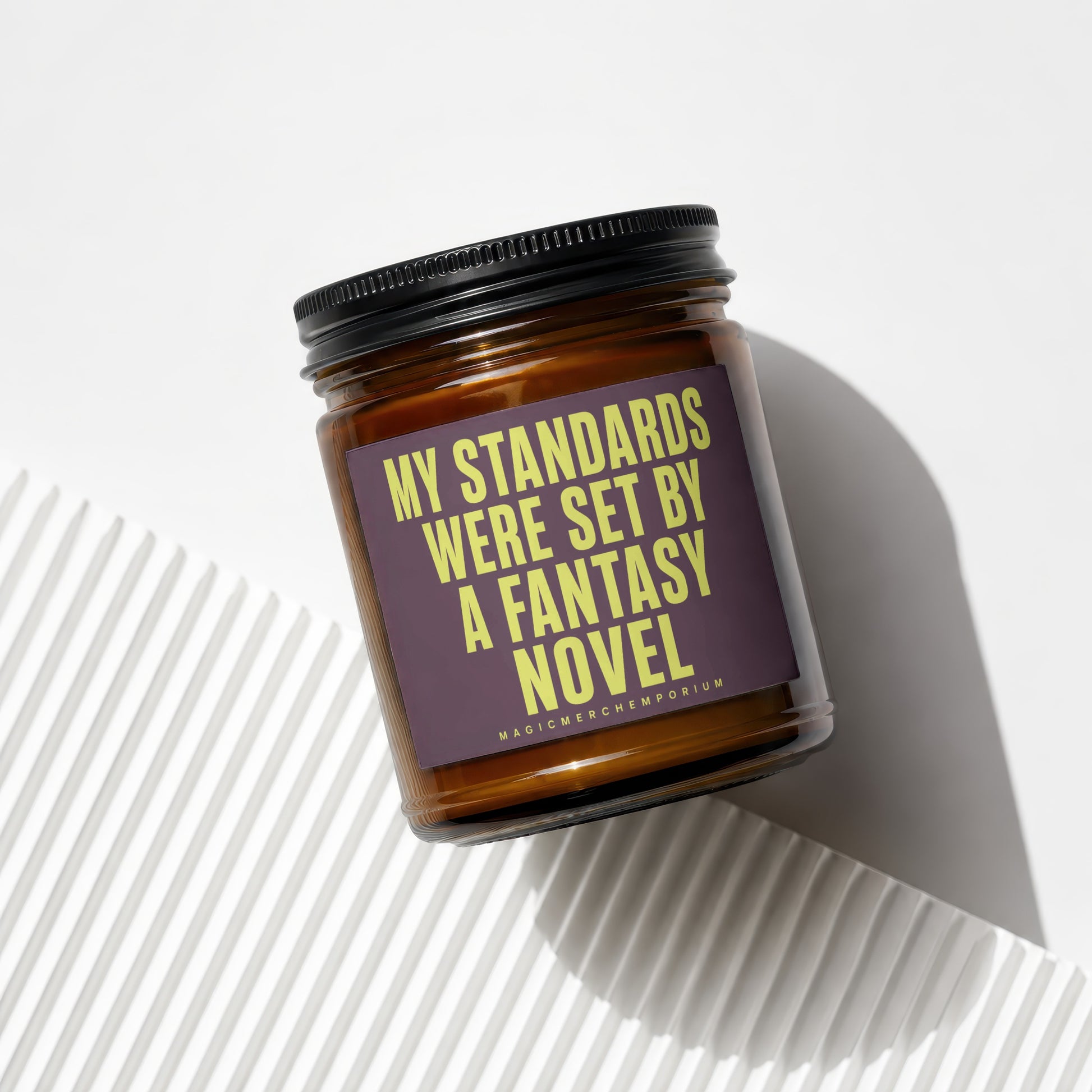 Amber candle with black lid and purple label reading "My standards were set by a fantasy novel".