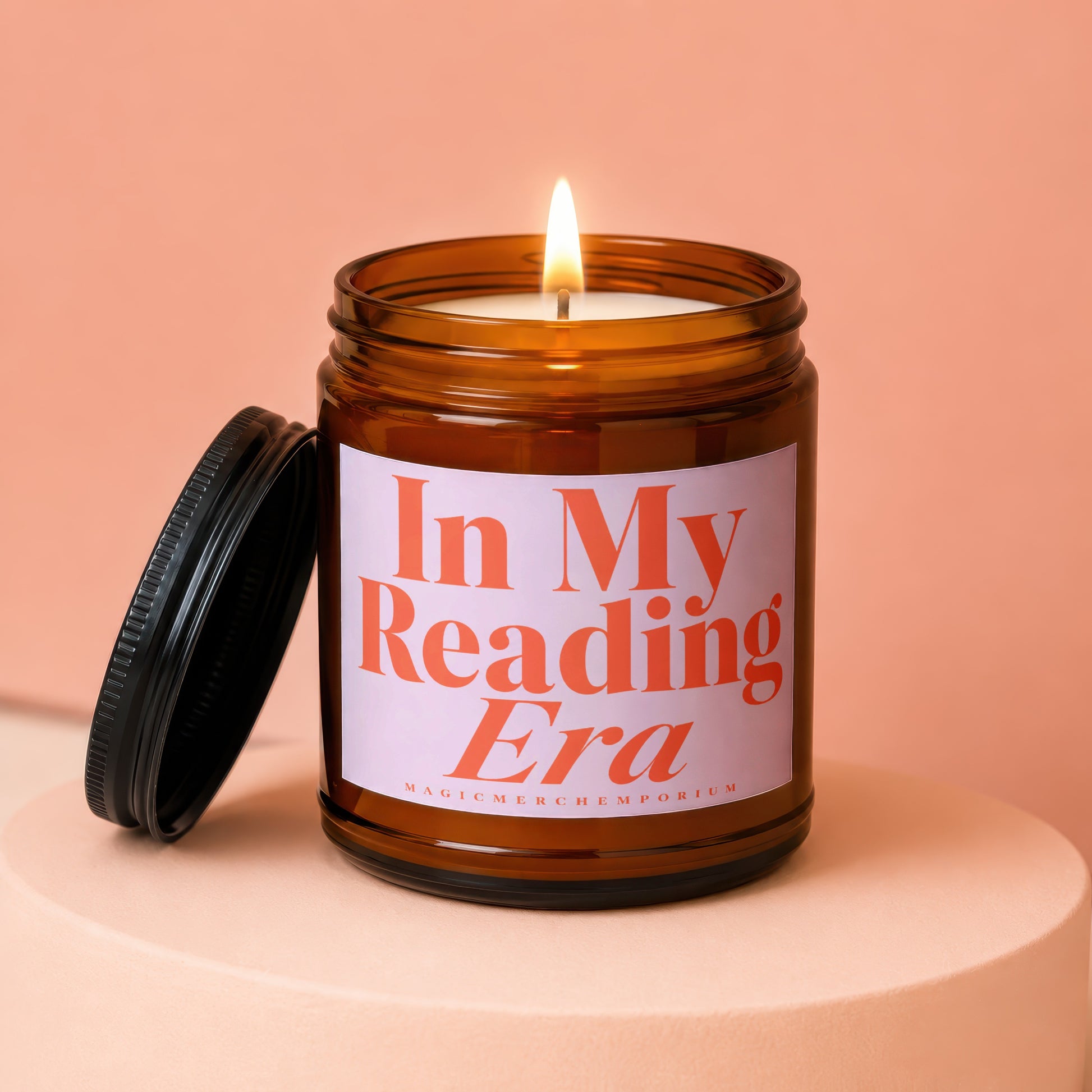Amber jar candle with lit wick and lid, reading "In My Reading Era".