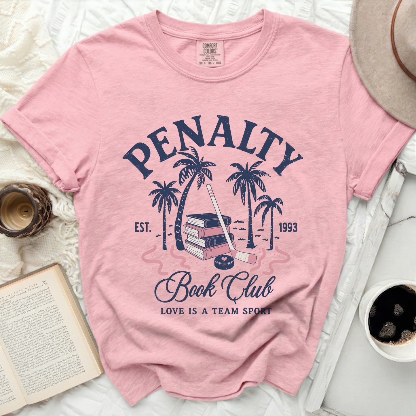Pink t-shirt with "Penalty Book Club" text, hockey stick, and palm trees.