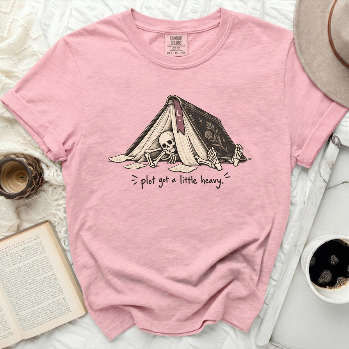 Pink t-shirt with skeleton under an open book graphic and text "plot got a little heavy."
