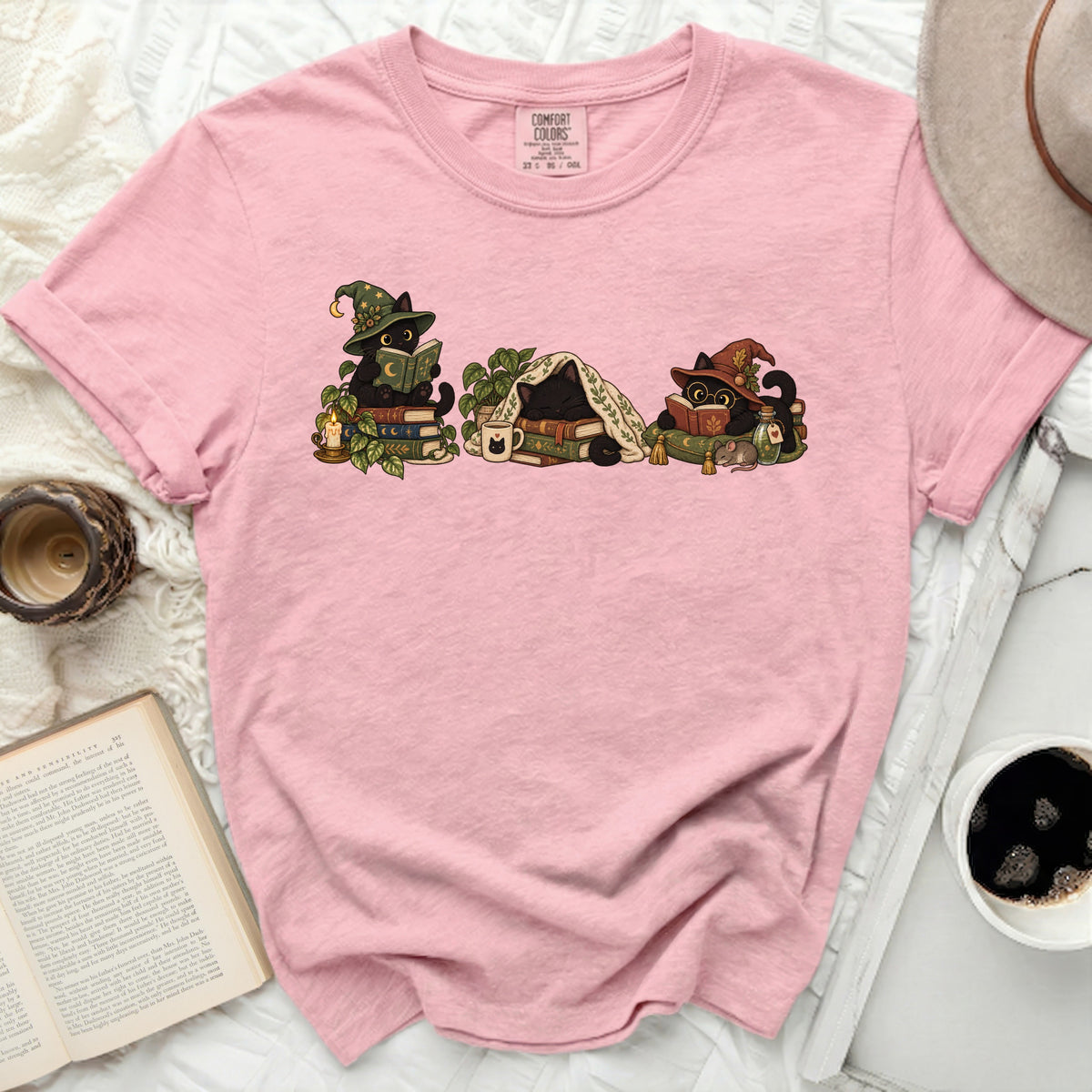 Pink t-shirt with a graphic of three black cats in witch hats reading books.
