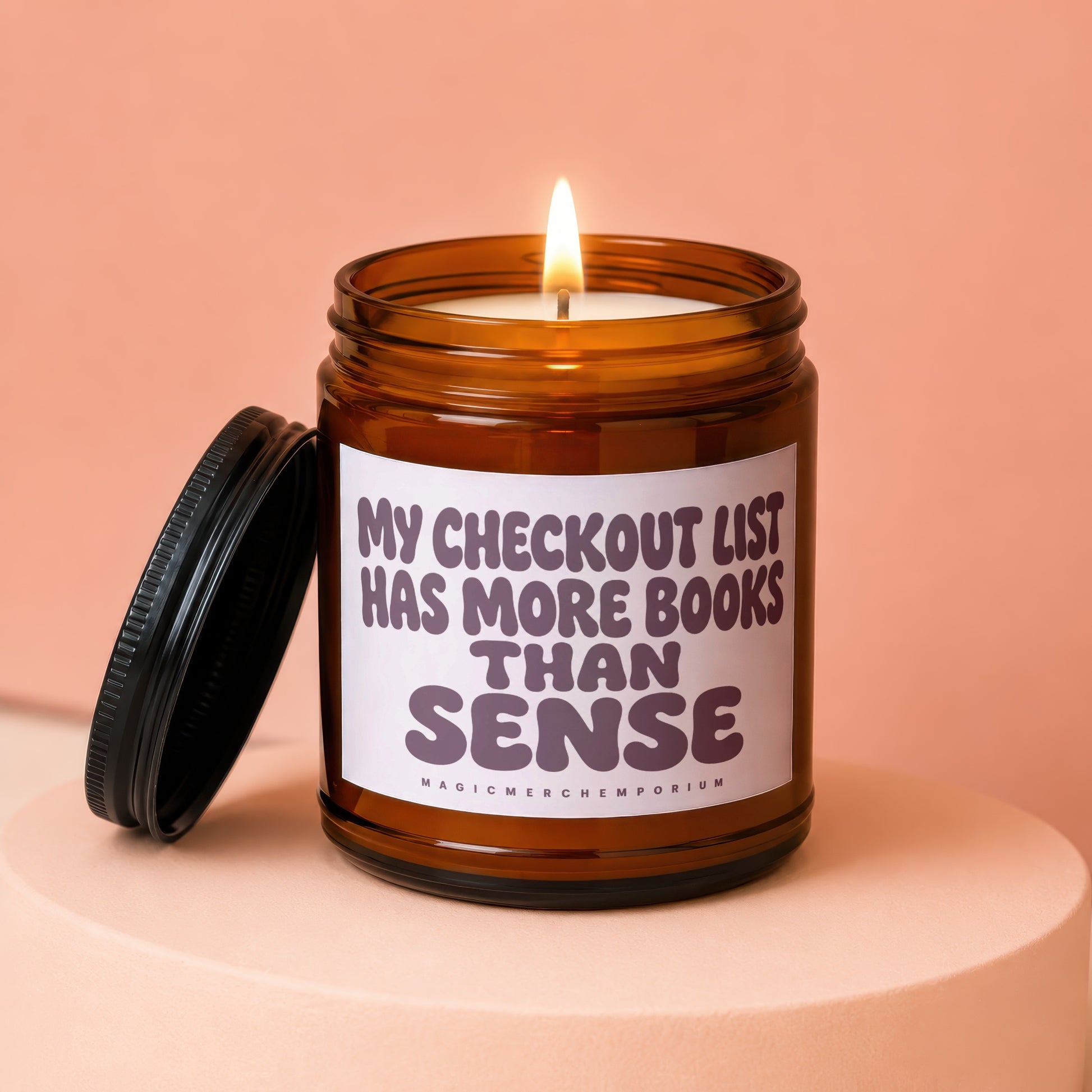 A lit amber jar candle with the text "MY CHECKOUT LIST HAS MORE BOOKS THAN SENSE".
