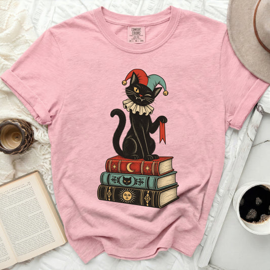 Black cat in jester hat sits on stack of books with moon, cat face, and sun designs.