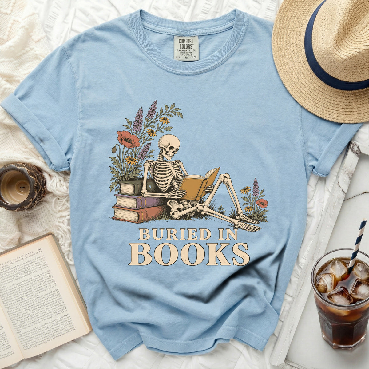 Light blue Comfort Colors shirt with skeleton reading book and text "BURIED IN BOOKS".