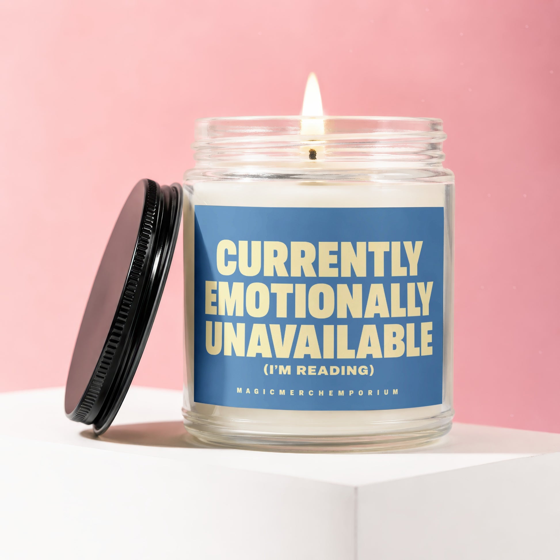 Glass candle with lit wick and label reading "Currently Emotionally Unavailable (I'm Reading)".