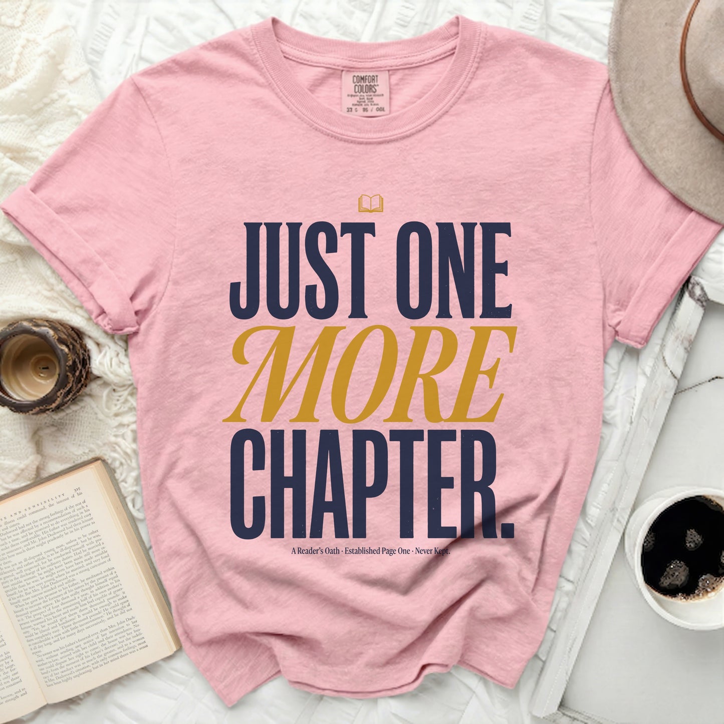 Pink t-shirt with "JUST ONE MORE CHAPTER" text in navy and gold.