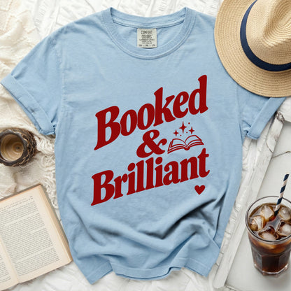 Light blue t-shirt with red text reading "Booked & Brilliant" and an open book graphic.