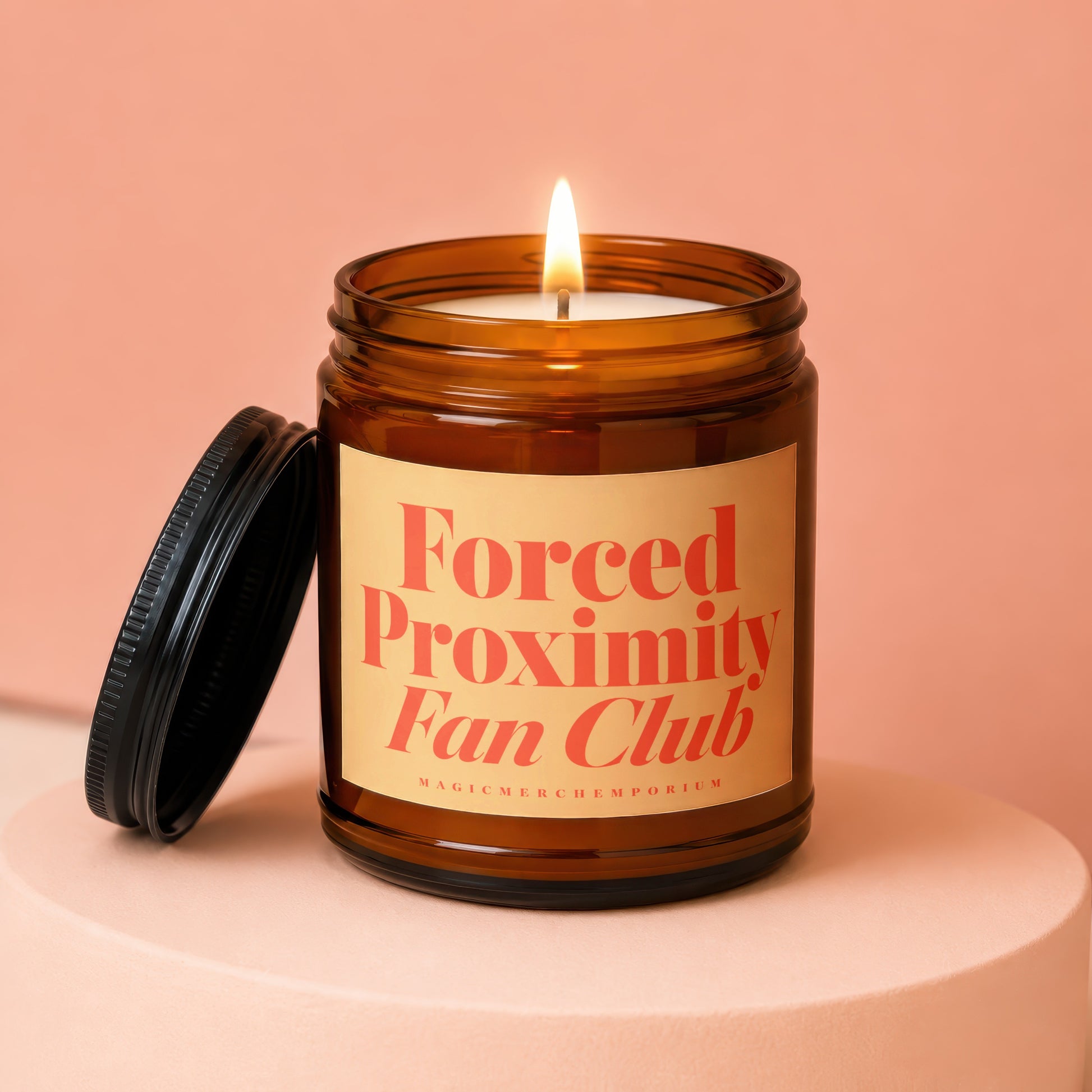 Amber glass candle with lit wick and black lid, labeled "Forced Proximity Fan Club".