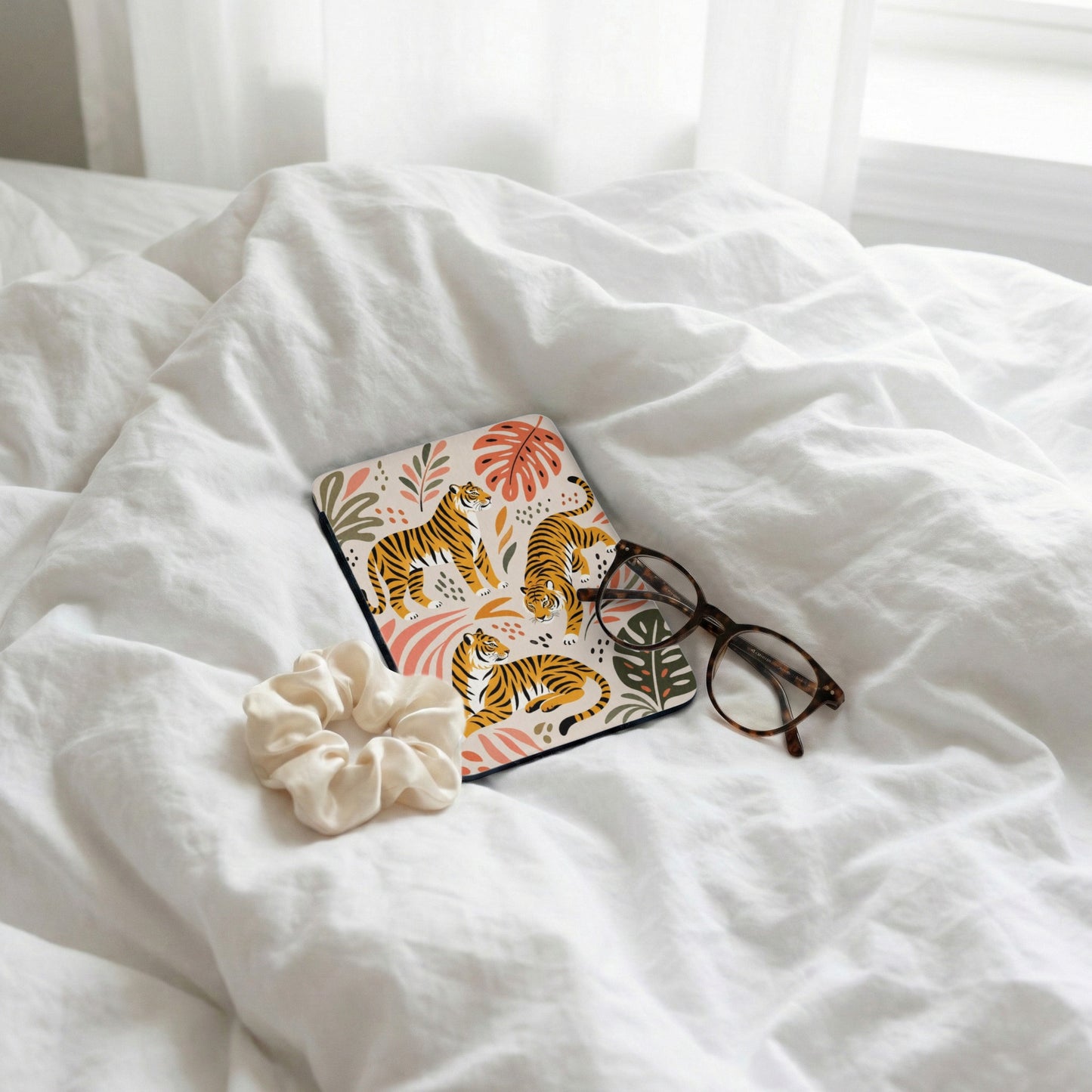 Coaster with tigers and tropical leaves pattern, scrunchie, and glasses on white bedding.
