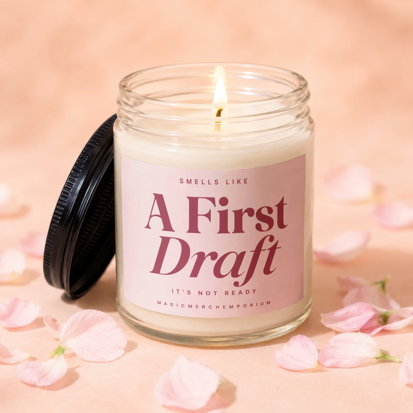 Lit candle in a glass jar with pink label reading "A First Draft".