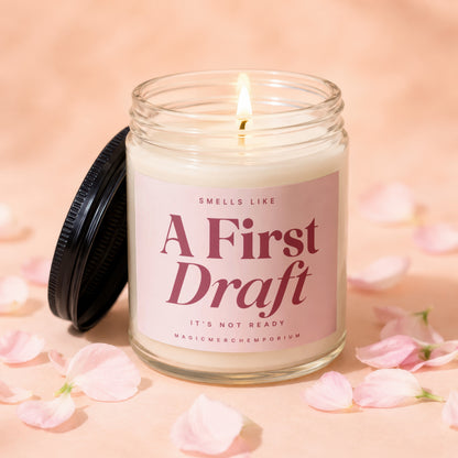 Lit candle in a glass jar with pink label reading "A First Draft".