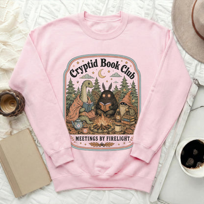 Pink sweatshirt with "Cryptid Book Club Meetings by Firelight" circular graphic.