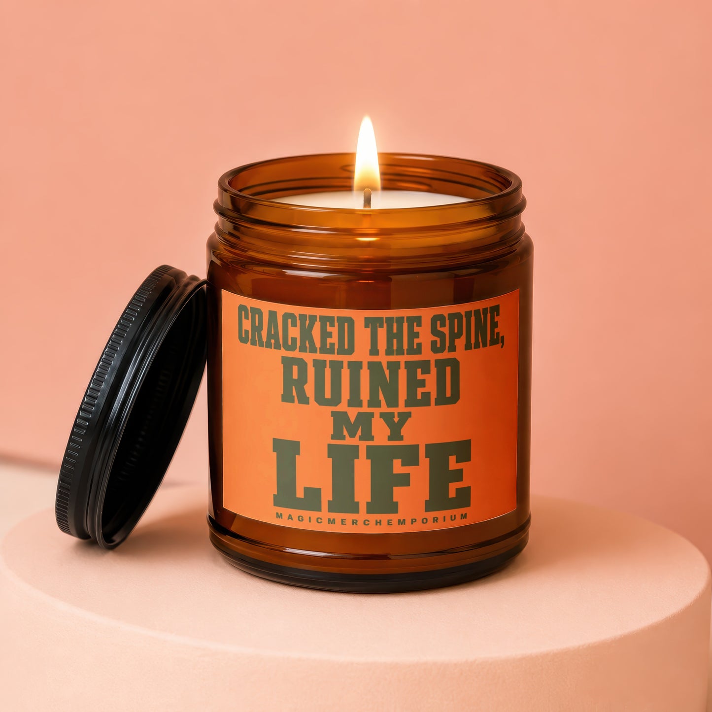 Amber jar candle with burning wick and black lid. Text reads: Cracked the Spine, Ruined My Life.