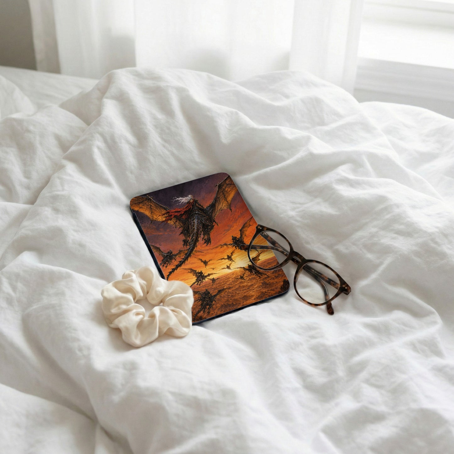 A phone case with dragons flying at sunset, beside glasses and a scrunchie.