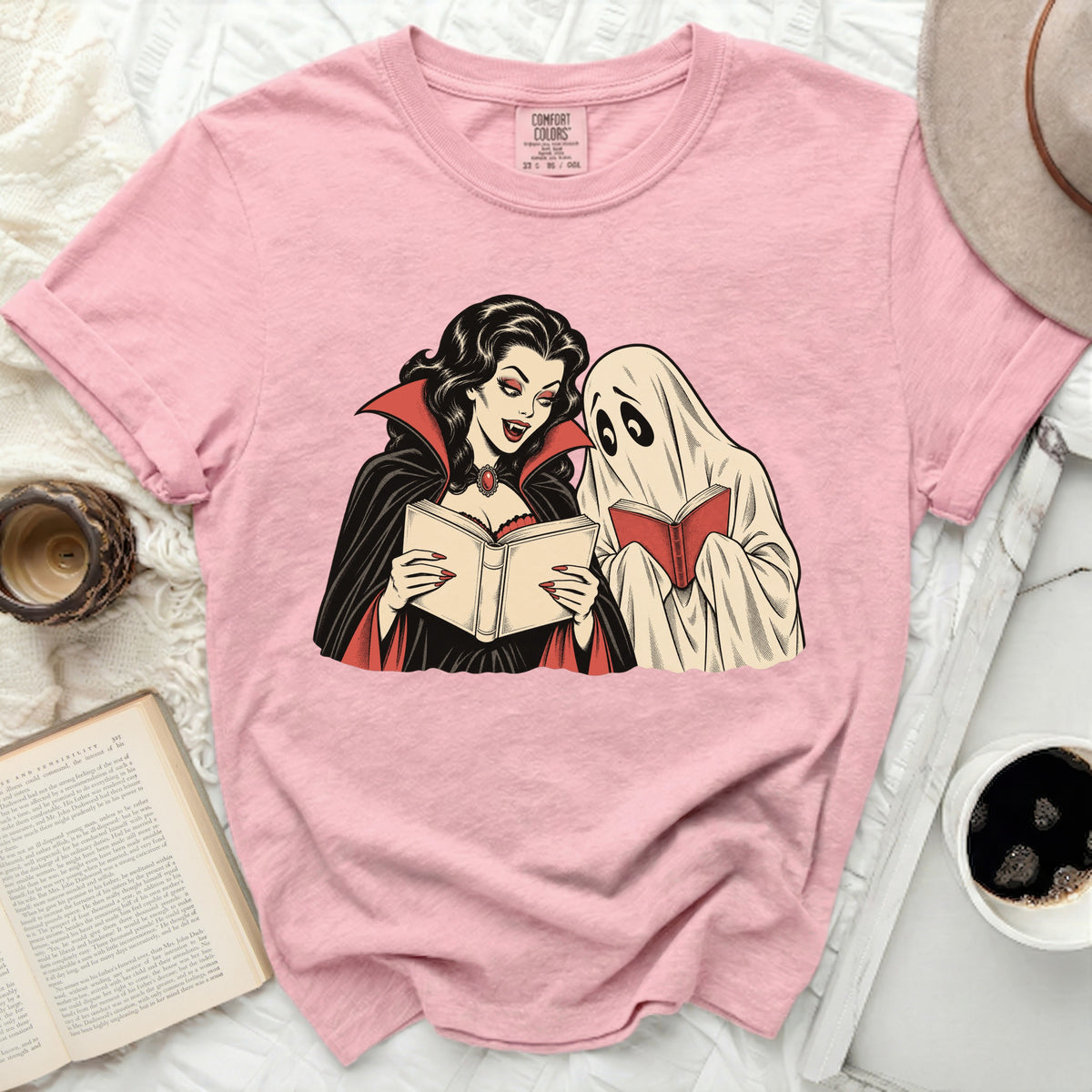 Pink t-shirt with graphic of a vampire and ghost reading books.