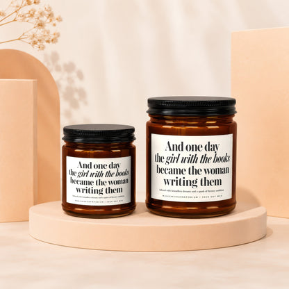 Two amber glass candles with white labels; quote: "And one day the girl with the books became the woman writing them."