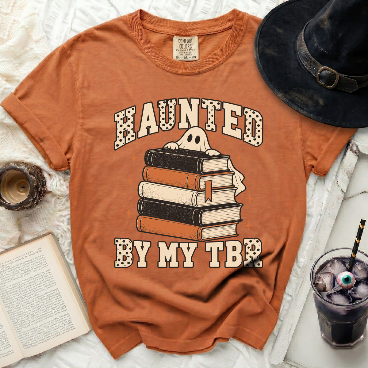 Orange t-shirt with ghost peeking over books and text "HAUNTED BY MY TBR."
