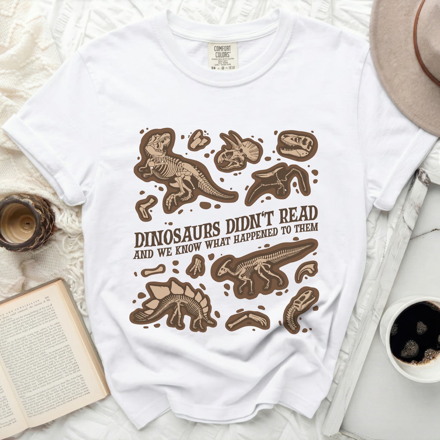 White t-shirt with brown dinosaur skeletons and text: Dinosaurs Didn't Read.