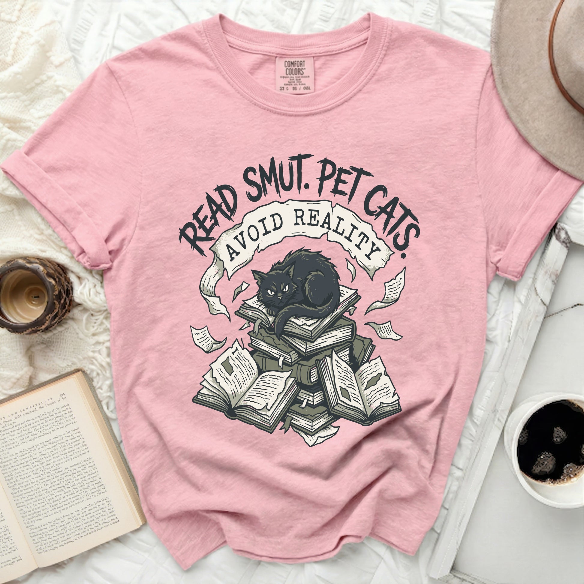 Pink t-shirt with black graphic of cat on books, text "Read Smut. Pet Cats. Avoid Reality."