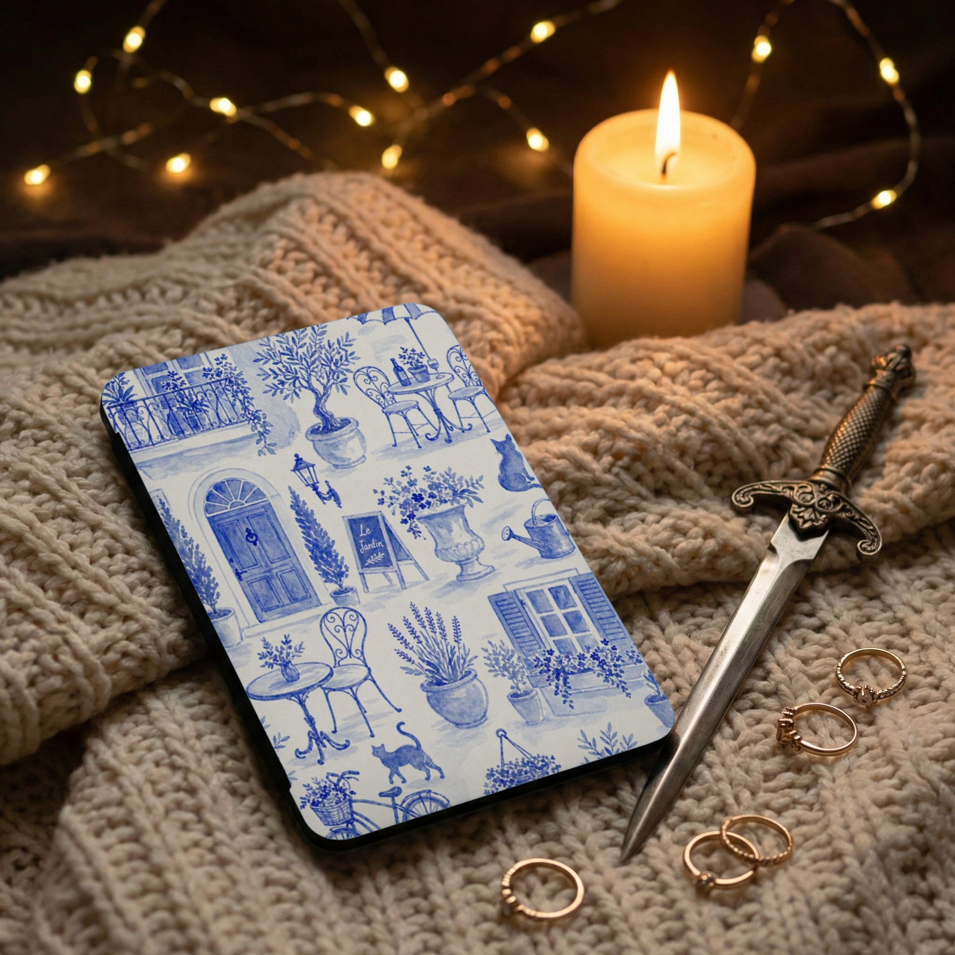 Blue and white toile phone case with outdoor cafe scene, a dagger, and rings.